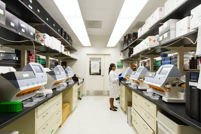 A woman in white lab coat standing next to a row of shelves.